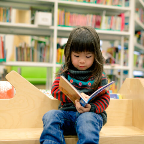 young girl reading book at library